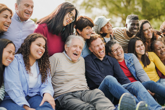 Large group of people from different generations smiling and enjoying time together outdoors.